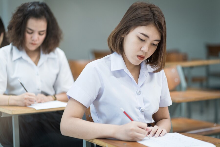 selective-focus-teenage-college-students-sit-lecture-chaire-write-examination-paper-answer-sheet-taking-final-examination-room-classroom-university-students-uniform-classroom_201468-559